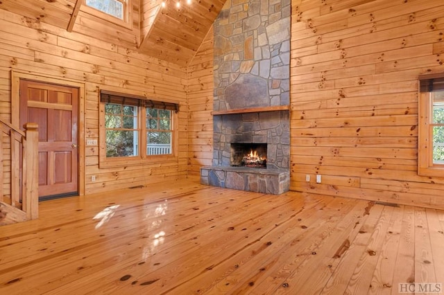 unfurnished living room with high vaulted ceiling, a fireplace, wooden walls, wooden ceiling, and light hardwood / wood-style flooring