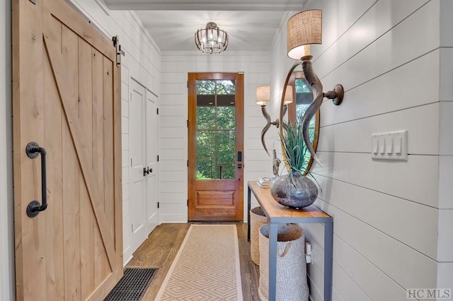 doorway to outside featuring wood-type flooring, a barn door, a chandelier, and wood walls