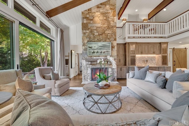 living room featuring a stone fireplace, beam ceiling, high vaulted ceiling, a barn door, and light hardwood / wood-style floors