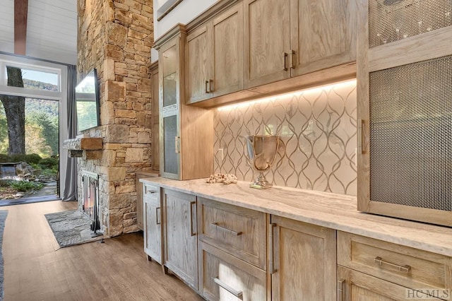 kitchen with a fireplace, backsplash, light stone countertops, light brown cabinets, and light hardwood / wood-style flooring