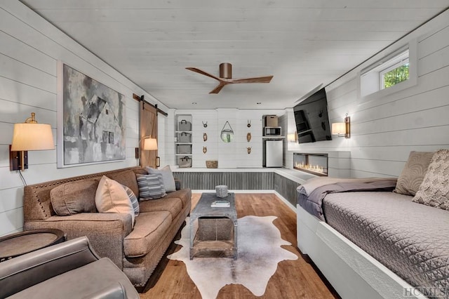 living room featuring a barn door, wood walls, ceiling fan, and light wood-type flooring