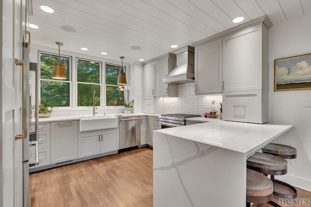 kitchen with custom exhaust hood, kitchen peninsula, pendant lighting, stainless steel appliances, and light stone countertops