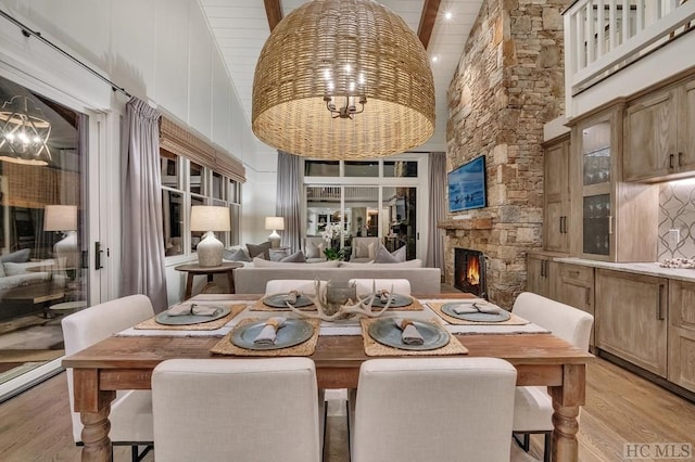 dining space with a fireplace, high vaulted ceiling, light hardwood / wood-style floors, and beamed ceiling