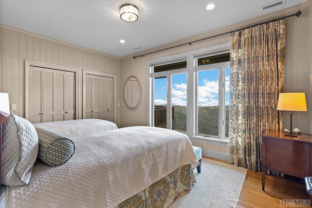 bedroom with crown molding, light hardwood / wood-style floors, and two closets