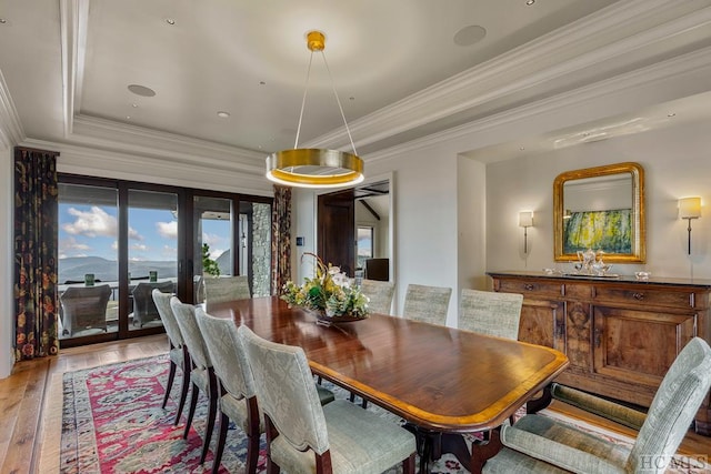 dining space with crown molding, a raised ceiling, and light wood-type flooring