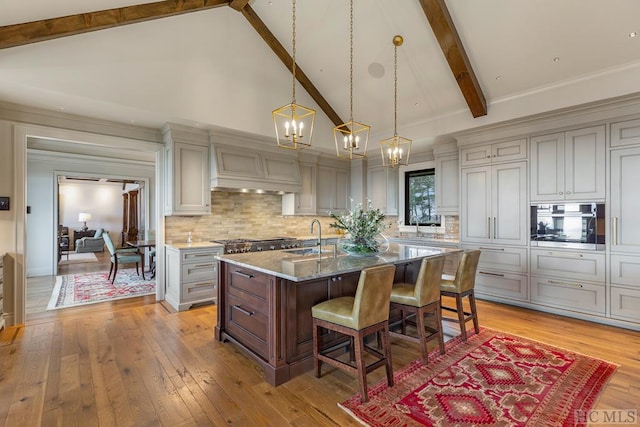 kitchen with beamed ceiling, gray cabinetry, a kitchen island with sink, and stone counters