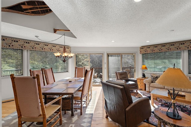 dining room featuring a healthy amount of sunlight, a textured ceiling, a notable chandelier, and light wood-type flooring