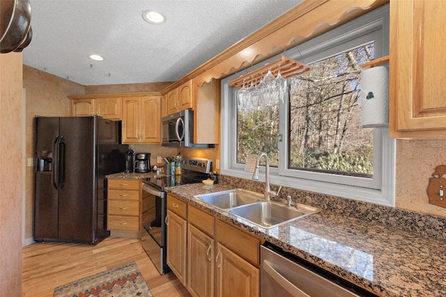 kitchen with sink, dark stone counters, light hardwood / wood-style floors, stainless steel appliances, and a textured ceiling