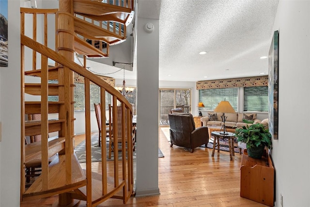 stairs featuring an inviting chandelier, wood-type flooring, and a textured ceiling