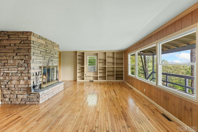 unfurnished living room with a fireplace, built in shelves, wooden walls, and light hardwood / wood-style flooring