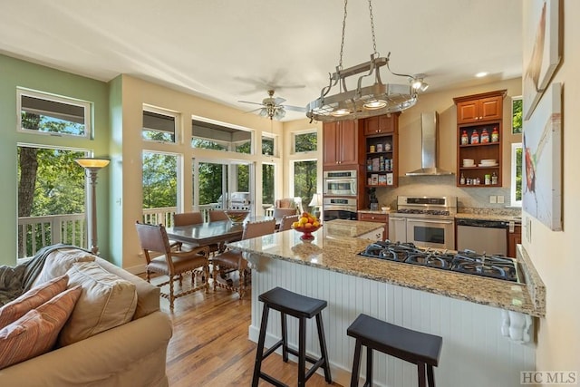 kitchen featuring decorative backsplash, wall chimney exhaust hood, stainless steel appliances, and light stone counters