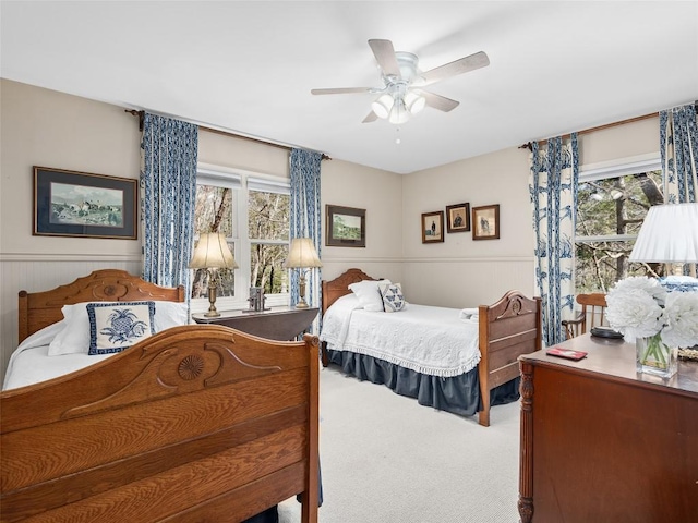 carpeted bedroom with a wainscoted wall, ceiling fan, and multiple windows