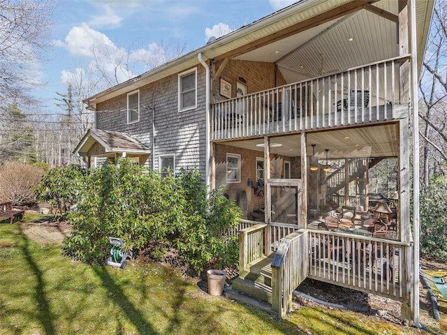 back of property with a balcony, a deck, a lawn, and stairs