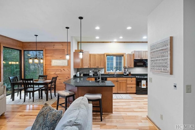 kitchen with light hardwood / wood-style flooring, black appliances, a breakfast bar area, and decorative light fixtures