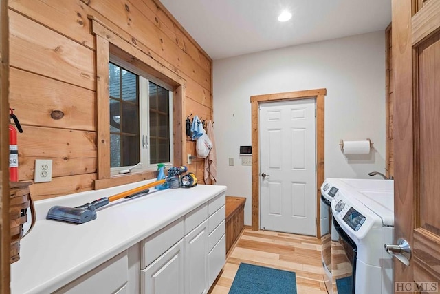 clothes washing area with wood walls, washer and clothes dryer, cabinets, and light hardwood / wood-style floors