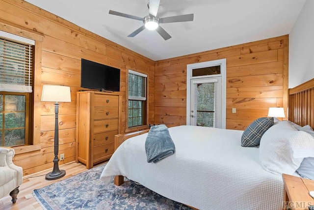 bedroom with light wood-type flooring, wooden walls, access to outside, and ceiling fan