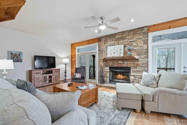 living room featuring light wood-type flooring, french doors, ceiling fan, and a fireplace