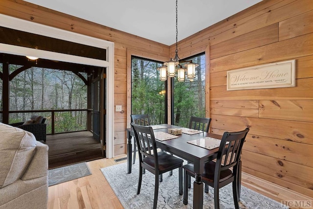 dining room with light hardwood / wood-style flooring, wooden walls, and a notable chandelier