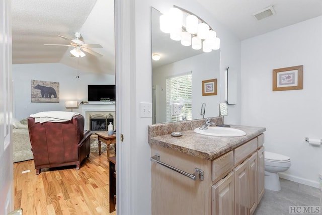 bathroom with lofted ceiling, toilet, vanity, hardwood / wood-style flooring, and ceiling fan