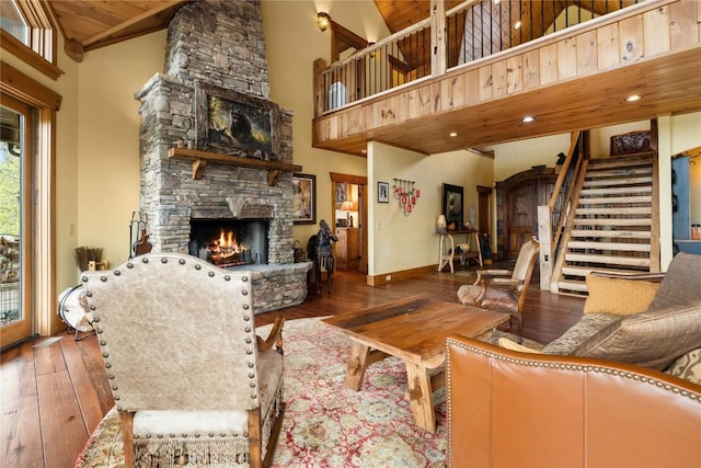 living room featuring a stone fireplace, hardwood / wood-style flooring, stairs, high vaulted ceiling, and baseboards