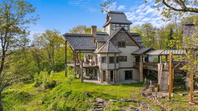 rear view of property with stairway, a deck, a standing seam roof, and a patio area