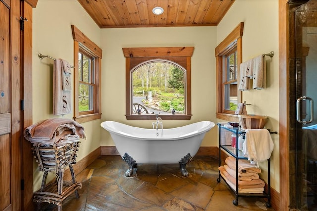 bathroom featuring stone tile flooring, baseboards, a soaking tub, wooden ceiling, and a stall shower
