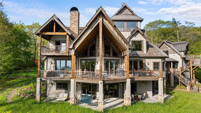 back of property with a patio, board and batten siding, a chimney, a lawn, and a balcony