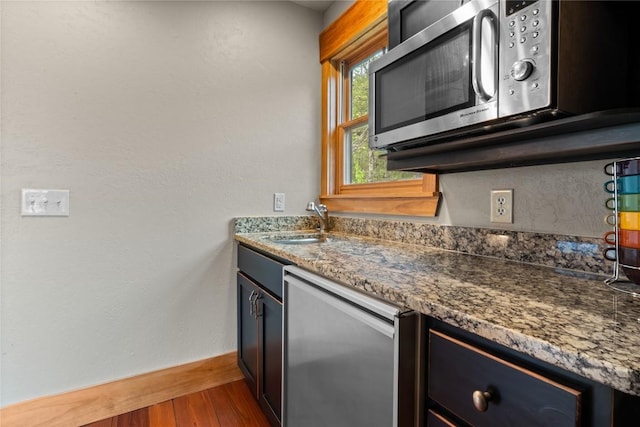 kitchen with stainless steel microwave, wood finished floors, refrigerator, a sink, and stone countertops
