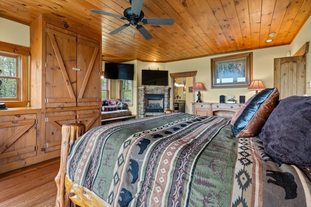 bedroom with wood ceiling, wood finished floors, and a stone fireplace