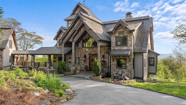 view of front of property featuring a standing seam roof, stone siding, a porch, a chimney, and metal roof