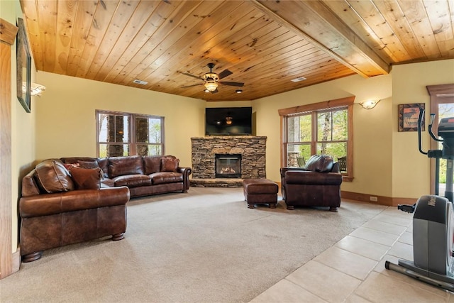 carpeted living room featuring tile patterned floors, wooden ceiling, a ceiling fan, a stone fireplace, and baseboards