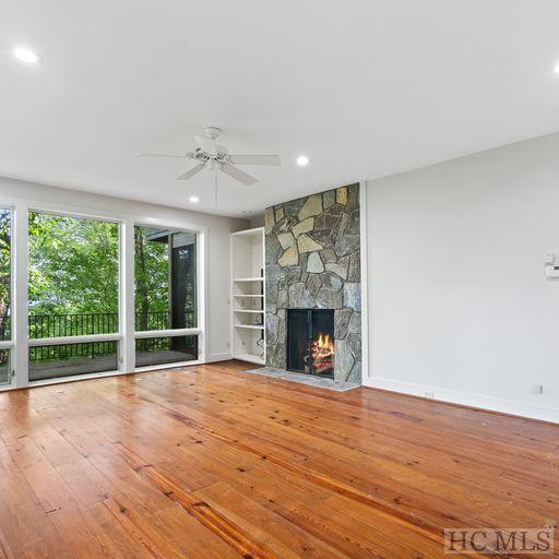 unfurnished living room with wood-type flooring, ceiling fan, and a stone fireplace