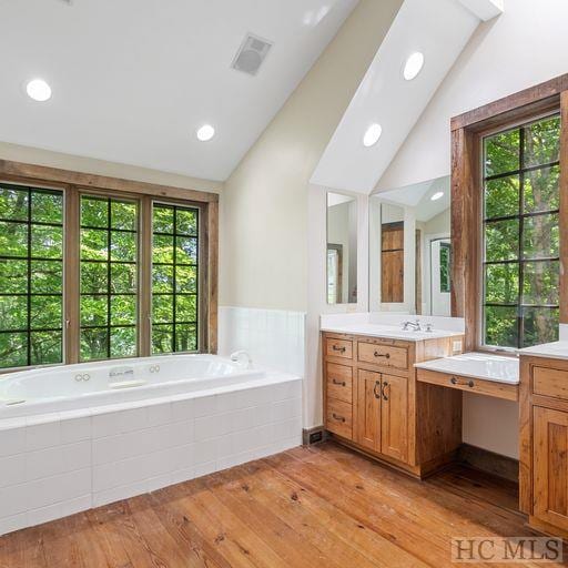 bathroom with a relaxing tiled tub, wood-type flooring, vanity, and lofted ceiling