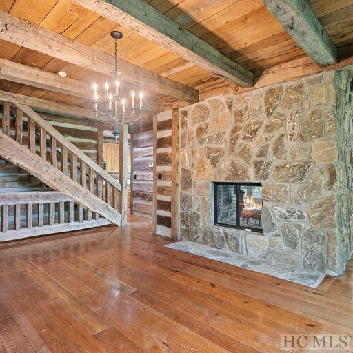 unfurnished living room featuring wood ceiling, a stone fireplace, an inviting chandelier, hardwood / wood-style flooring, and beam ceiling