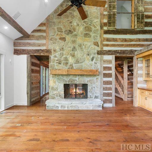 unfurnished living room with a stone fireplace, ceiling fan, hardwood / wood-style flooring, high vaulted ceiling, and beam ceiling