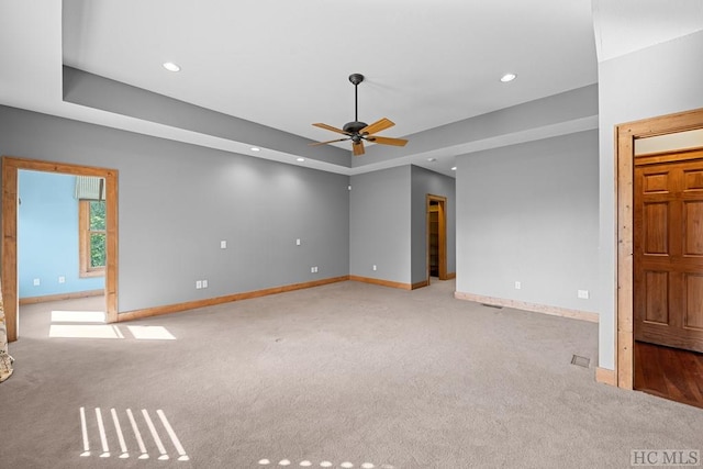 carpeted spare room with a raised ceiling and ceiling fan