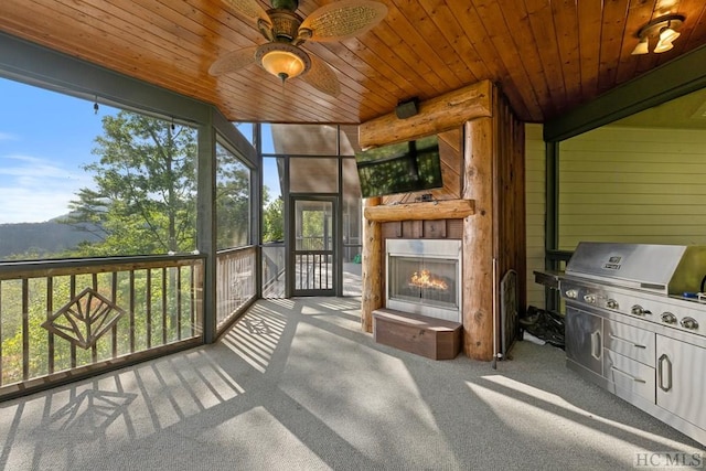 sunroom featuring an outdoor fireplace, plenty of natural light, ceiling fan, and wood ceiling