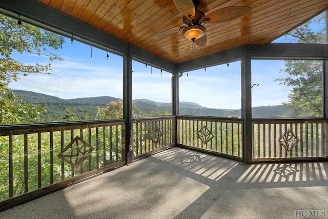 unfurnished sunroom featuring ceiling fan, a mountain view, and wooden ceiling