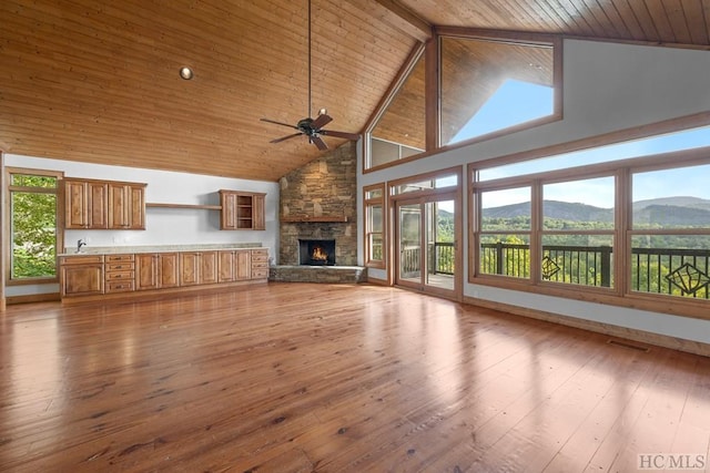 unfurnished living room featuring a stone fireplace, high vaulted ceiling, ceiling fan, light hardwood / wood-style floors, and a mountain view