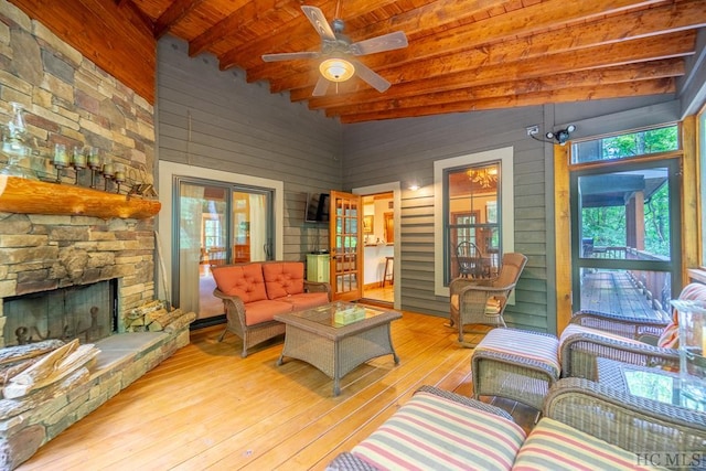 living room featuring wooden walls, lofted ceiling with beams, a stone fireplace, wooden ceiling, and light wood-type flooring