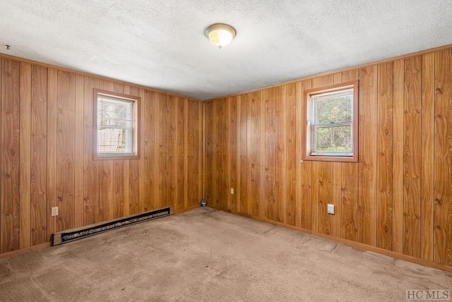 unfurnished room featuring wood walls, a textured ceiling, a baseboard radiator, and light colored carpet