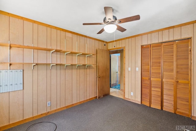 unfurnished bedroom featuring dark carpet, ceiling fan, a closet, and wooden walls