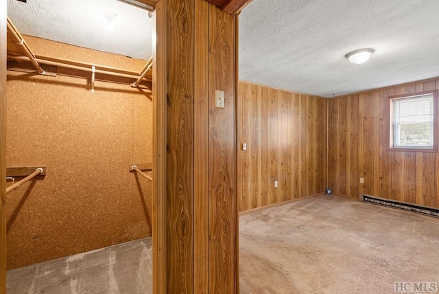 basement featuring carpet, a textured ceiling, a baseboard heating unit, and wooden walls