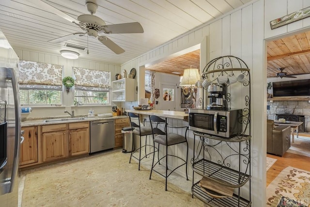 kitchen featuring appliances with stainless steel finishes, a stone fireplace, sink, ceiling fan, and a breakfast bar