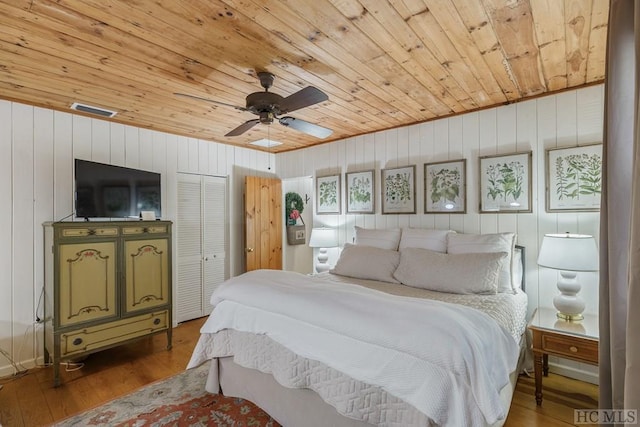 bedroom with ceiling fan, wood walls, hardwood / wood-style floors, wood ceiling, and a closet