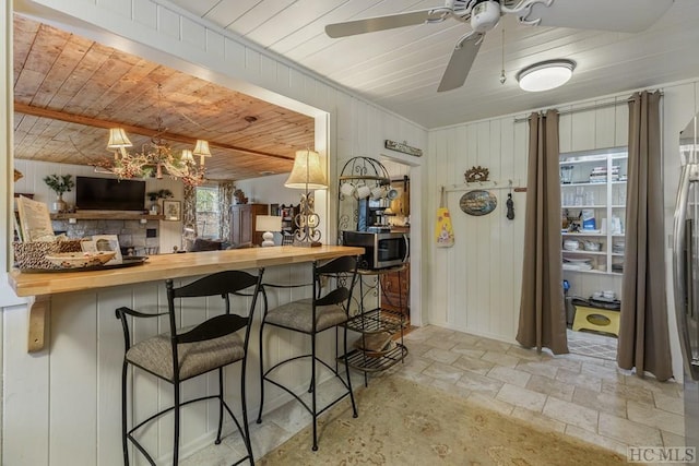 kitchen featuring a kitchen bar, kitchen peninsula, wood walls, butcher block countertops, and ceiling fan with notable chandelier