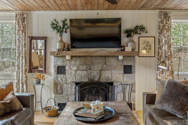 living room featuring light wood-type flooring, wooden walls, a stone fireplace, and wooden ceiling