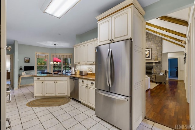 kitchen featuring vaulted ceiling with beams, decorative light fixtures, light tile patterned floors, appliances with stainless steel finishes, and cream cabinets