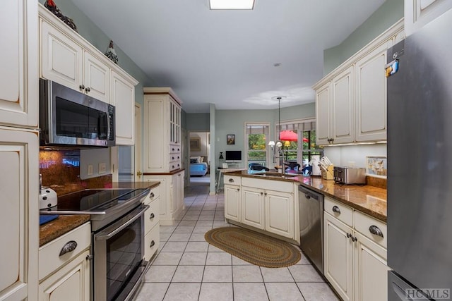 kitchen with sink, hanging light fixtures, dark stone countertops, light tile patterned floors, and stainless steel appliances