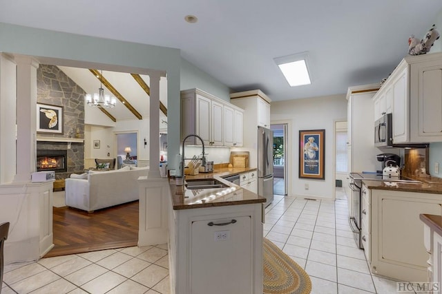 kitchen with appliances with stainless steel finishes, sink, white cabinets, light tile patterned floors, and kitchen peninsula